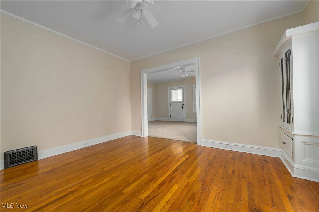 Empty room with crown molding, light wood-style flooring, and a ceiling fan