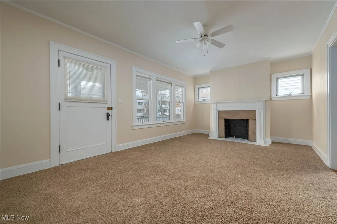 Unfurnished living room with crown molding, a fireplace with flush hearth, light colored carpet, and ceiling fan