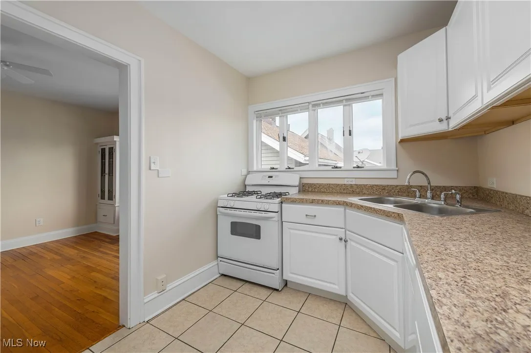 Kitchen with white range with gas cooktop, white cabinets, light countertops, and light tile patterned flooring