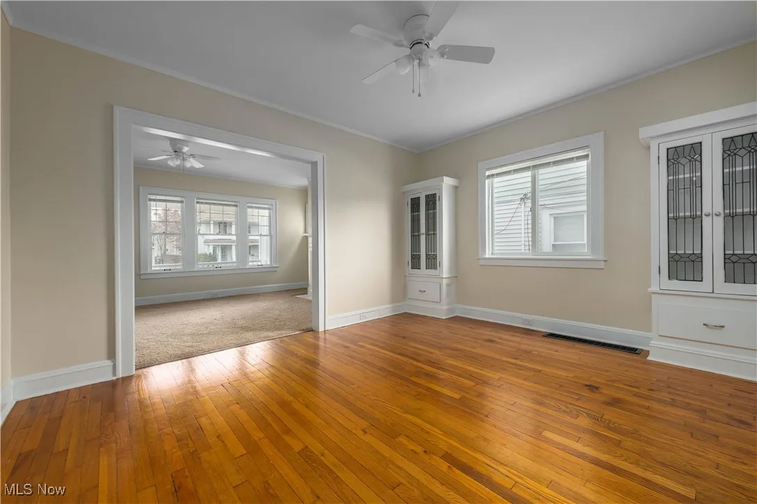 Empty room with light wood-style floors, healthy amount of natural light, crown molding, and ceiling fan