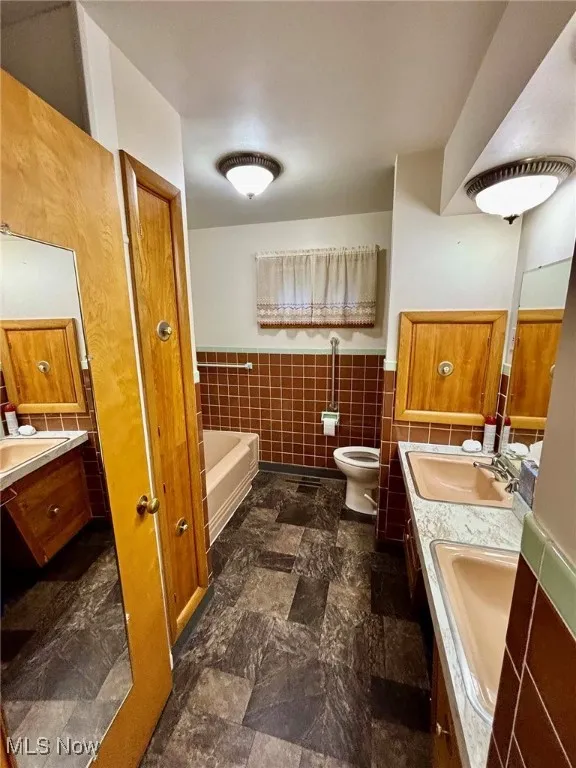 Main level bathroom with double vanity, a wainscoted wall, a bath, and tile walls