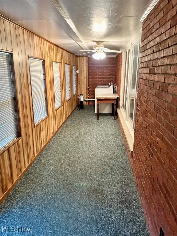 Enclosed porch with carpet flooring, brick wall, ceiling fan, wooden walls, and a textured ceiling
