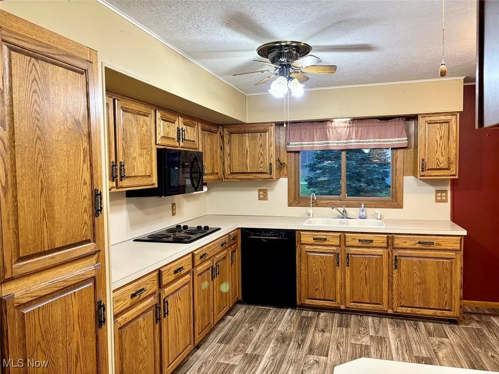 Kitchen with black appliances, wood finished floors, light countertops, ceiling fan, and brown cabinets