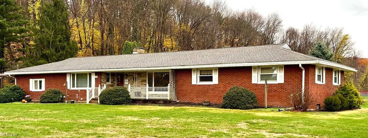 Ranch-style home featuring a porch, a front lawn, brick siding, and a chimney