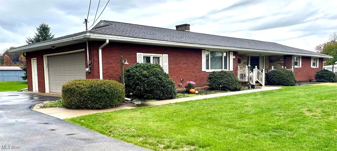 Single story home featuring a front yard, a chimney, an attached garage, brick siding, and a porch