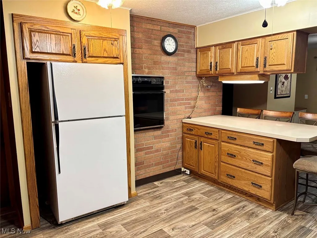 Kitchen with a peninsula, a kitchen bar, freestanding refrigerator, light countertops, and a textured ceiling