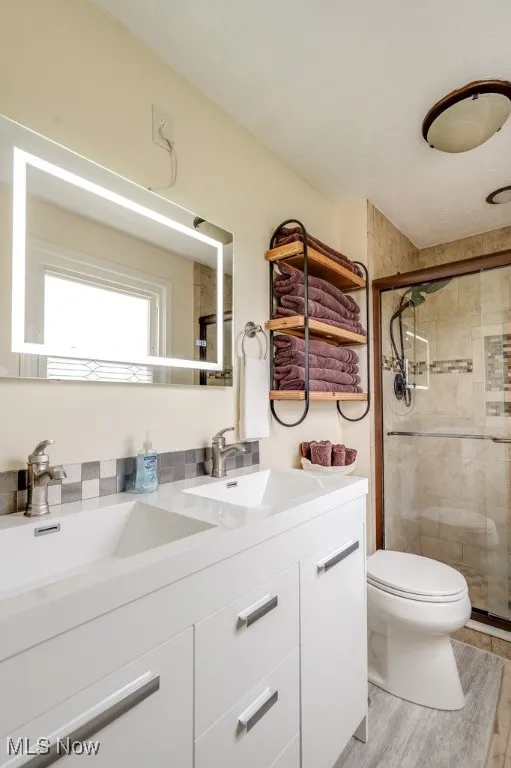 Full bath featuring double vanity, a shower stall, and light wood finished floors