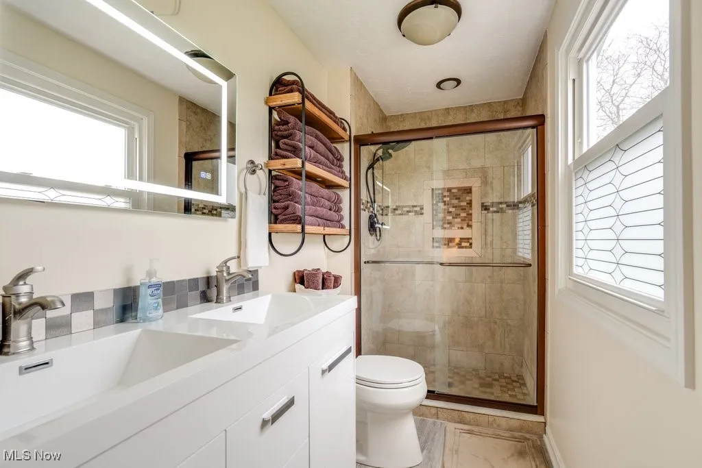 Full bath featuring double vanity, a shower stall, and plenty of natural light