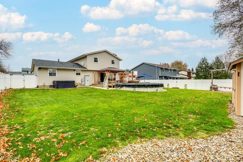 Rear view of property with a gazebo, a fenced backyard, a jacuzzi, and a patio