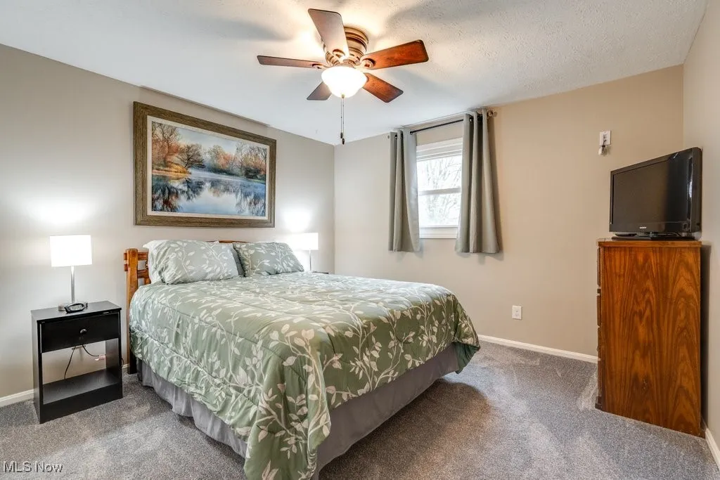 Carpeted bedroom featuring ceiling fan and a textured ceiling