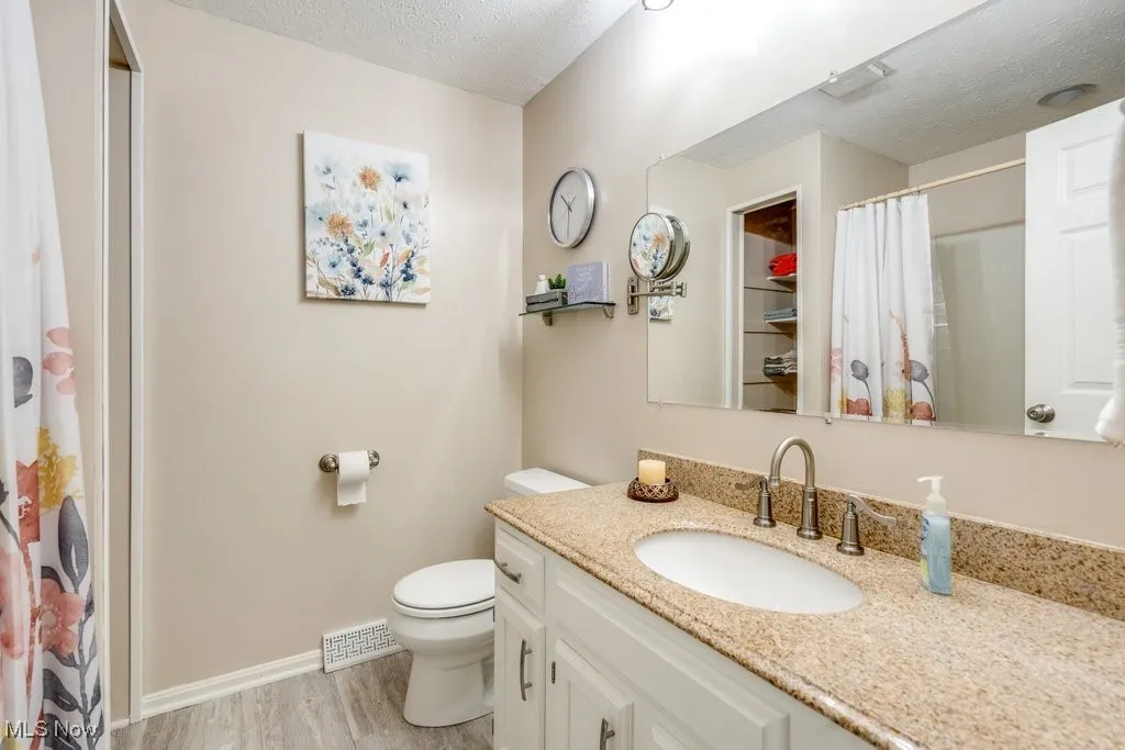 Full bath with a shower with curtain, a textured ceiling, vanity, and light wood-style floors