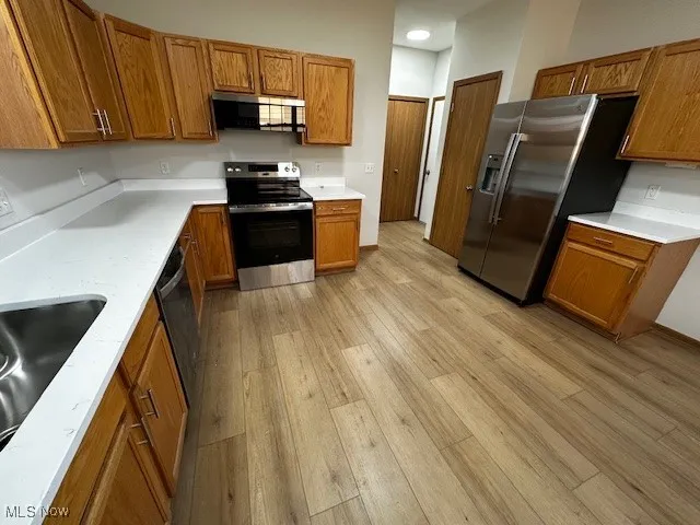 Kitchen with brown cabinetry, appliances with stainless steel finishes, and light wood-type flooring