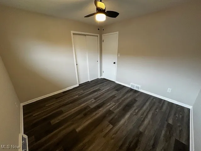 Unfurnished bedroom featuring dark wood-style flooring, ceiling fan, and a closet