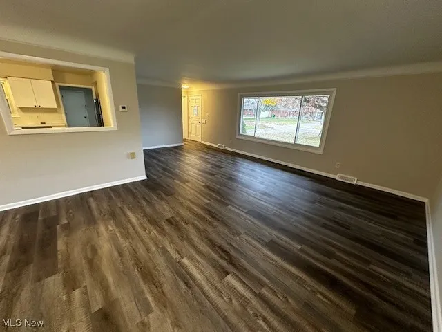 Unfurnished living room featuring dark wood-style flooring and crown molding