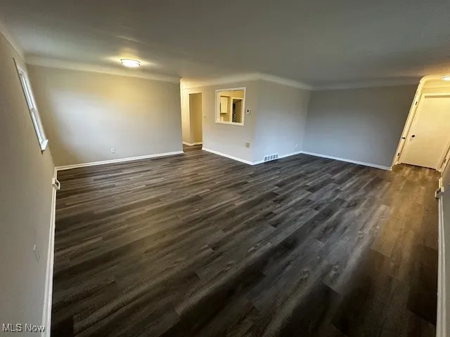 Spare room featuring dark wood-style flooring and crown molding
