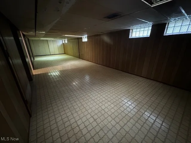 Basement featuring wooden walls, a drop ceiling, and tile patterned floors