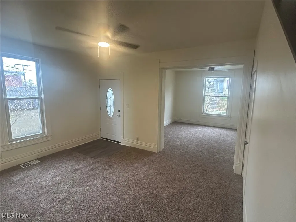 Carpeted foyer entrance with plenty of natural light and a ceiling fan
