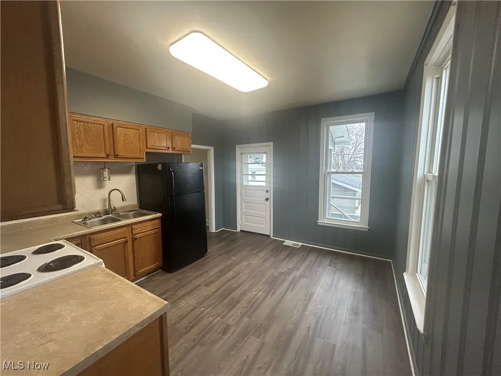 Kitchen featuring light countertops, brown cabinetry, freestanding refrigerator, white range with electric cooktop, and dark wood-style flooring