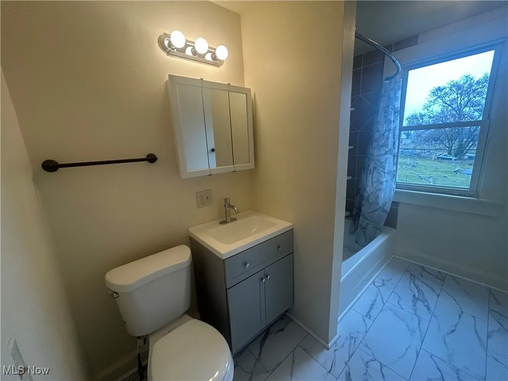 Bathroom featuring light marble finish floors, shower / tub combo, and vanity
