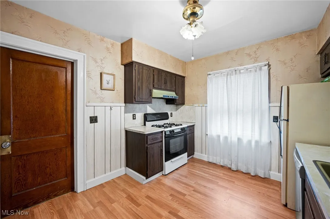 Kitchen with wallpapered walls, a wainscoted wall, dark brown cabinets, and light countertops