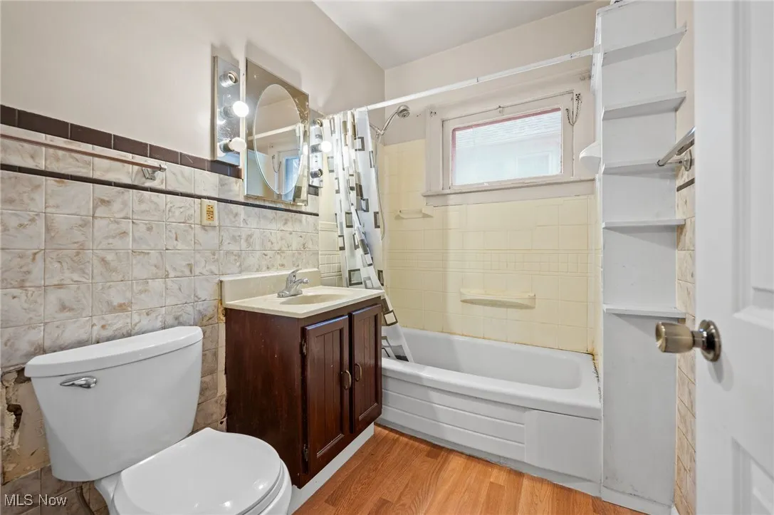 Bathroom featuring shower / bath combination with curtain, vanity, light wood style floors, and tile walls