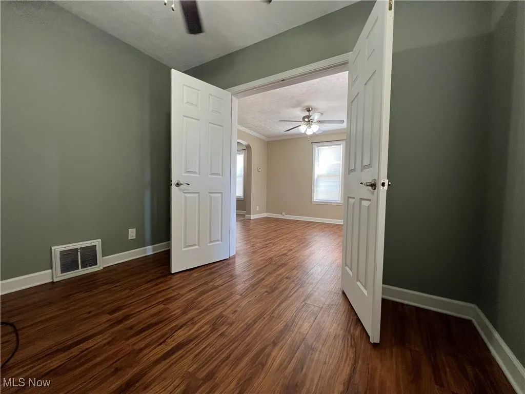 Spare room featuring a ceiling fan, dark wood-style flooring, ornamental molding, and arched walkways