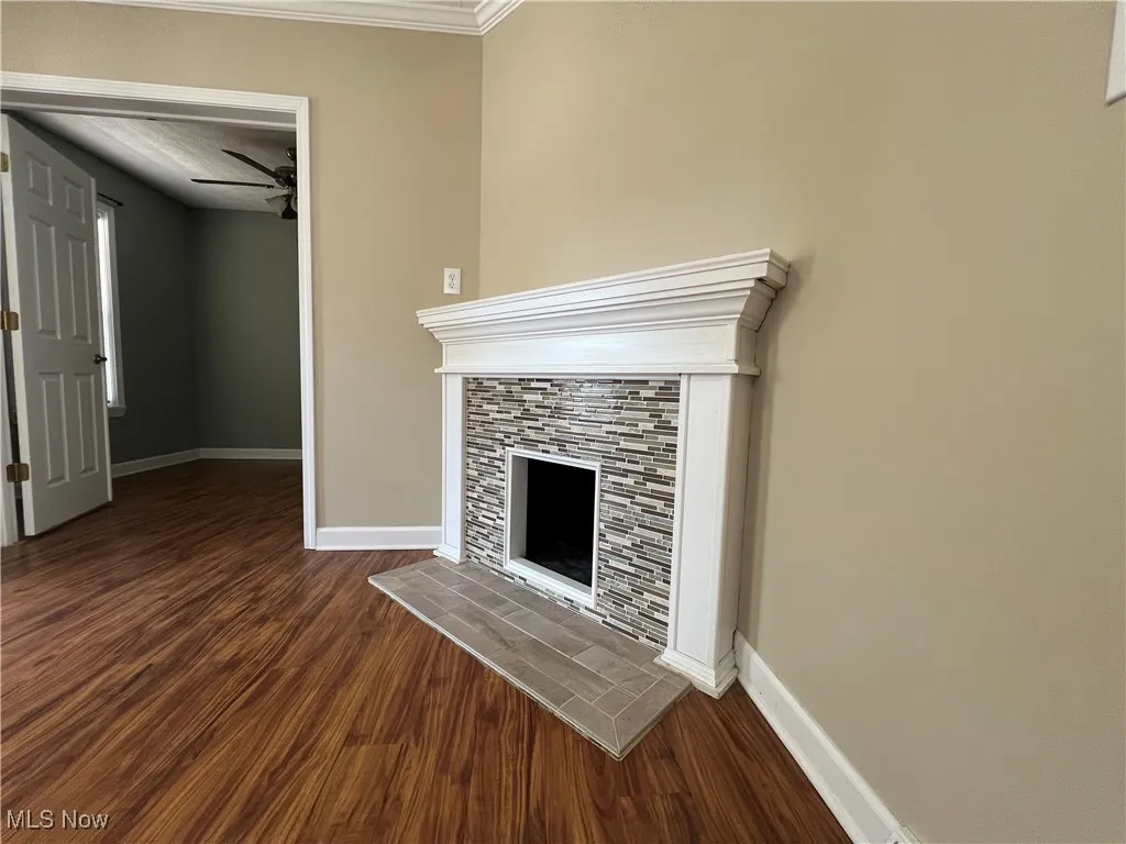 Unfurnished living room featuring dark wood-style floors, a fireplace, crown molding, and ceiling fan