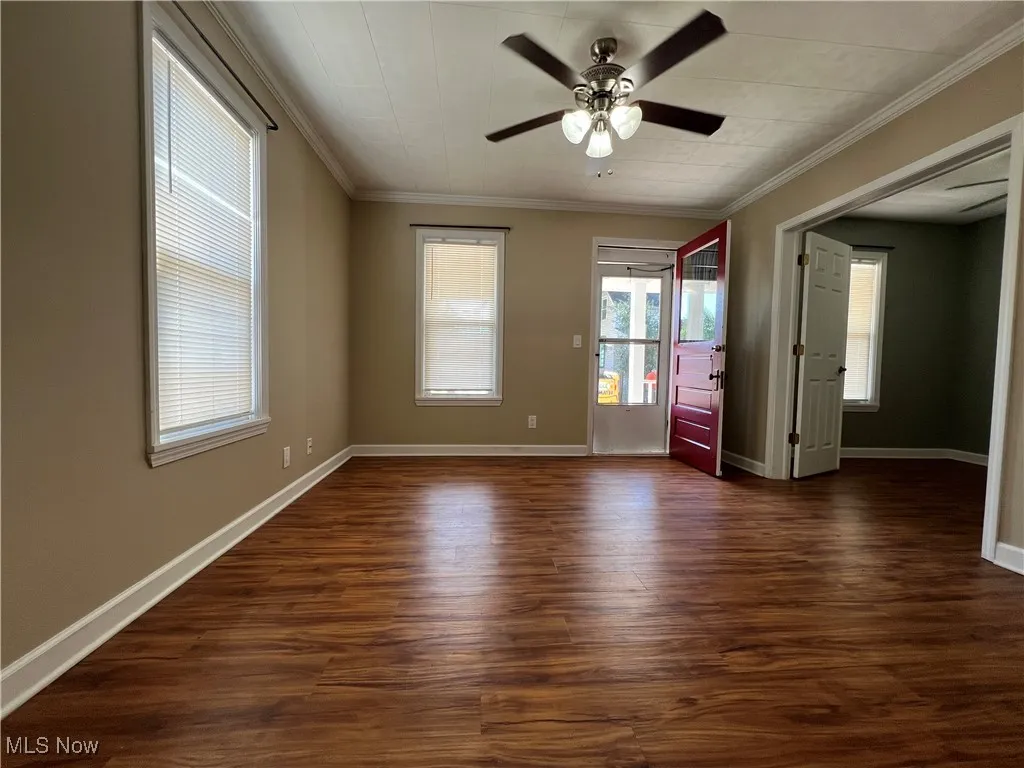 Empty room featuring dark wood-style floors, ornamental molding, and ceiling fan