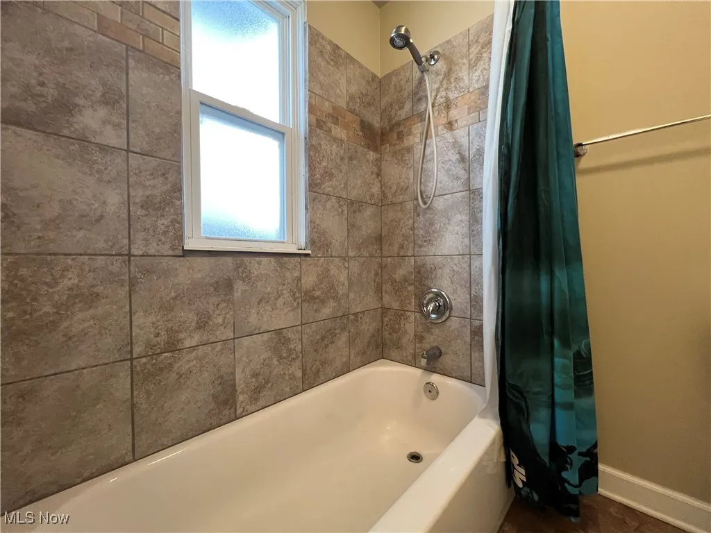 Bathroom with shower / bathtub combination with curtain and baseboards