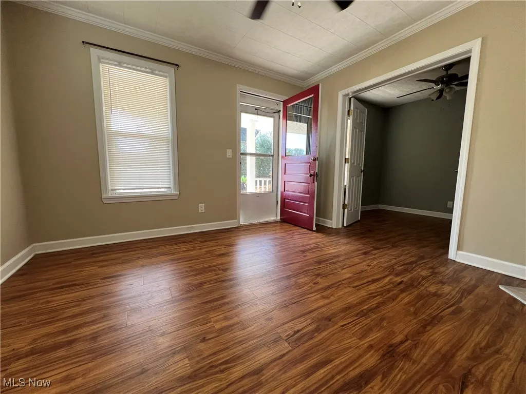 Unfurnished bedroom with dark wood-style floors, crown molding, and ceiling fan