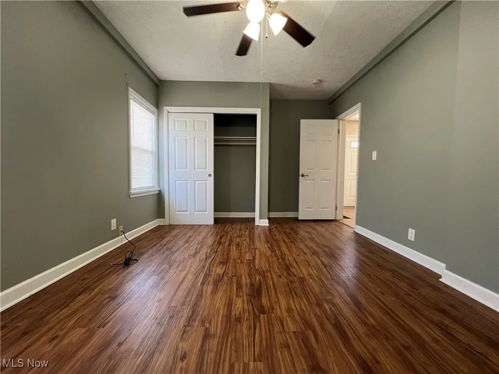 Unfurnished bedroom with dark wood-style floors, a textured ceiling, ceiling fan, and a closet