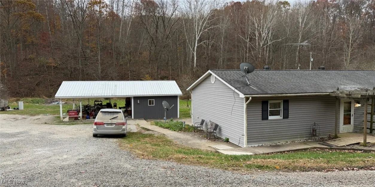View of front of house featuring roof with shingles, driveway, and a forest view