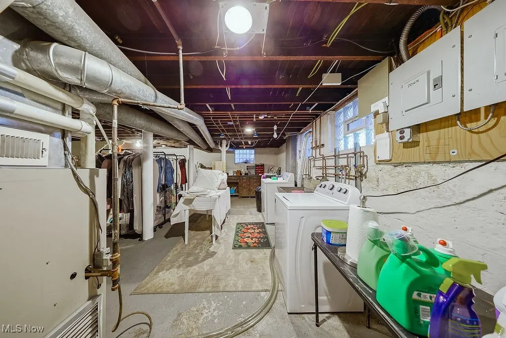 Basement featuring electric panel, heating unit, and washer and dryer