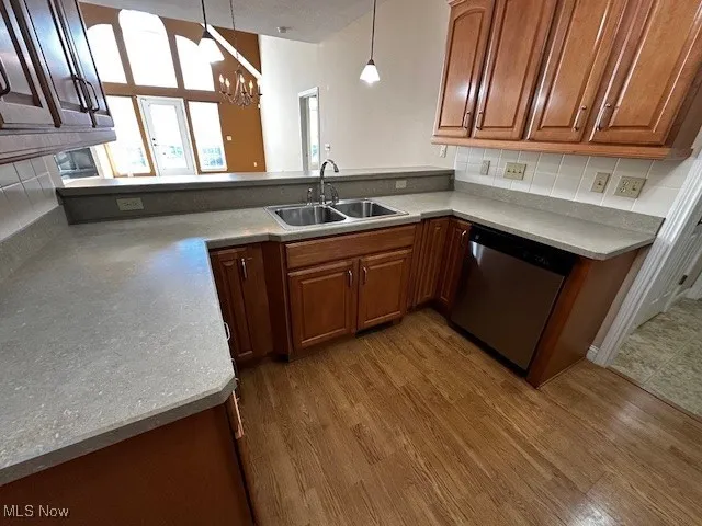 Kitchen featuring brown cabinets, hanging light fixtures, dishwasher, a chandelier, and dark wood finished floors