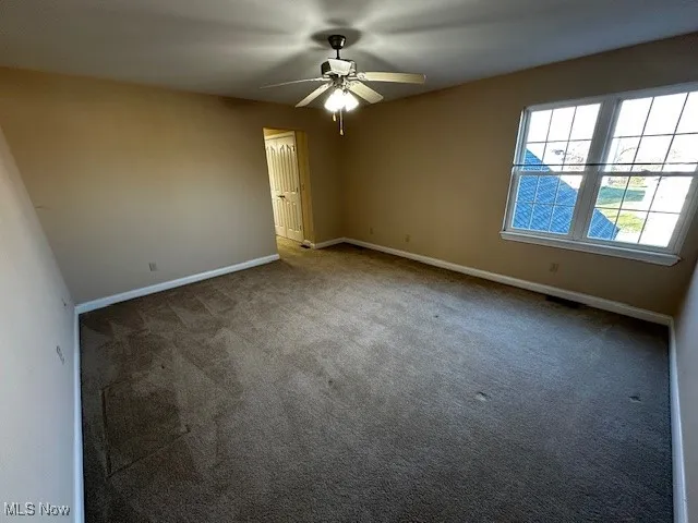 Carpeted empty room featuring baseboards and ceiling fan
