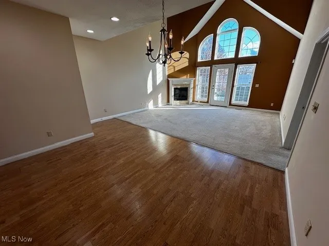 Unfurnished living room with a glass covered fireplace, a chandelier, high vaulted ceiling, dark wood finished floors, and recessed lighting