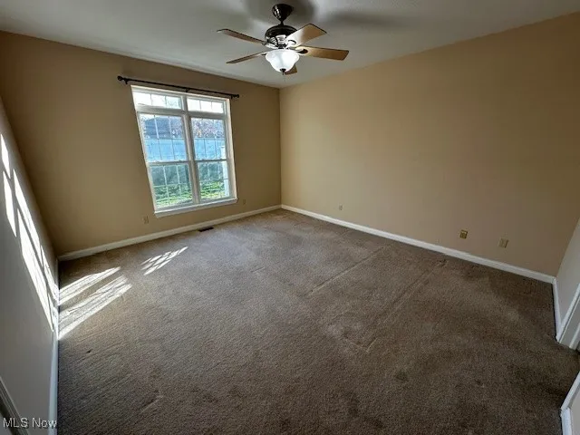 Carpeted spare room featuring baseboards and a ceiling fan