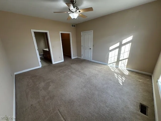Unfurnished bedroom featuring a walk in closet, ceiling fan, ensuite bath, and carpet