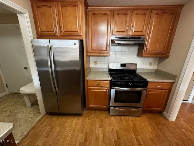 Kitchen featuring stainless steel appliances, brown cabinets, light countertops, tasteful backsplash, and light wood-type flooring