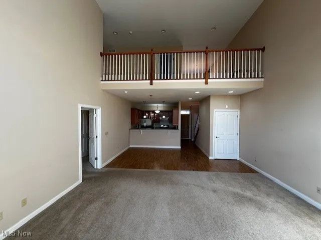 Unfurnished living room featuring dark carpet and a high ceiling