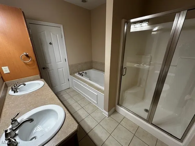Full bath featuring double vanity, a stall shower, light tile patterned floors, and a bath