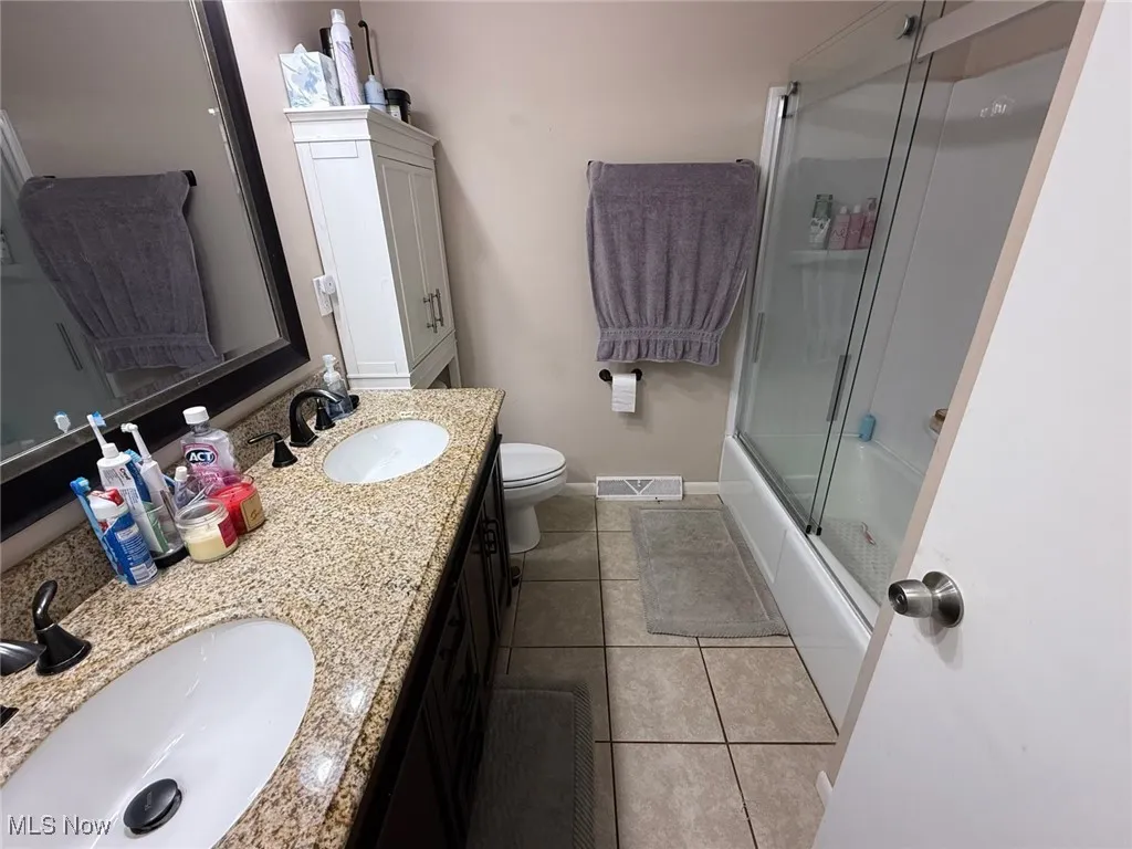Bathroom with double vanity, light tile patterned floors, and combined bath / shower with glass door