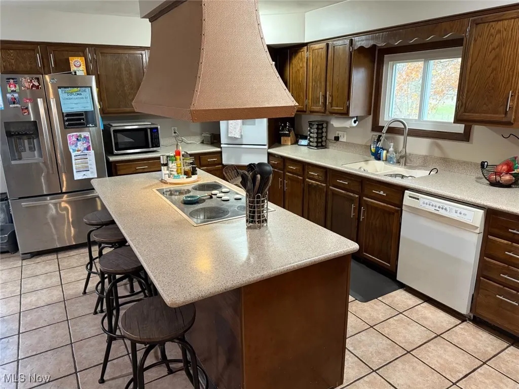 Kitchen featuring a kitchen breakfast bar, stainless steel appliances, a center island, dark brown cabinets, and light tile patterned floors