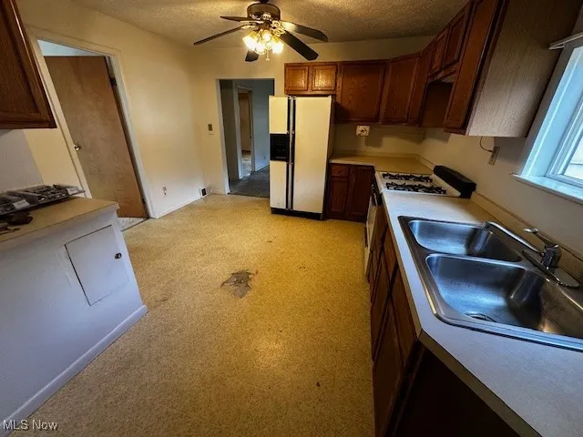 Kitchen featuring light countertops, ceiling fan, white appliances, a textured ceiling, and light floors