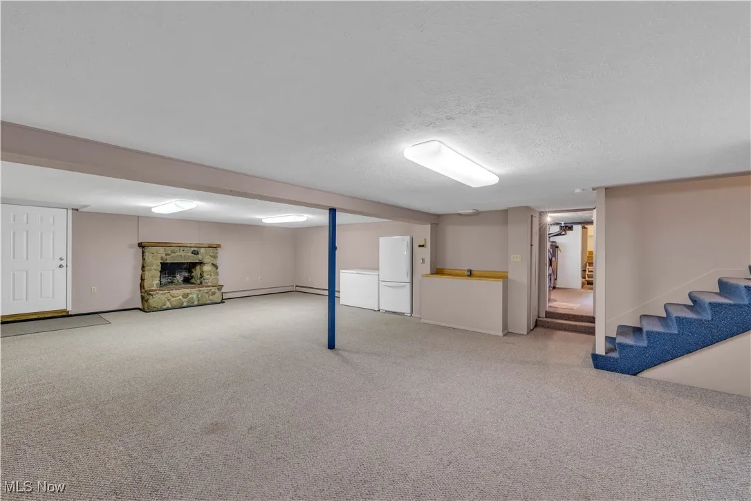 Finished below grade area featuring freestanding refrigerator, stairs, a fireplace, light colored carpet, and a textured ceiling