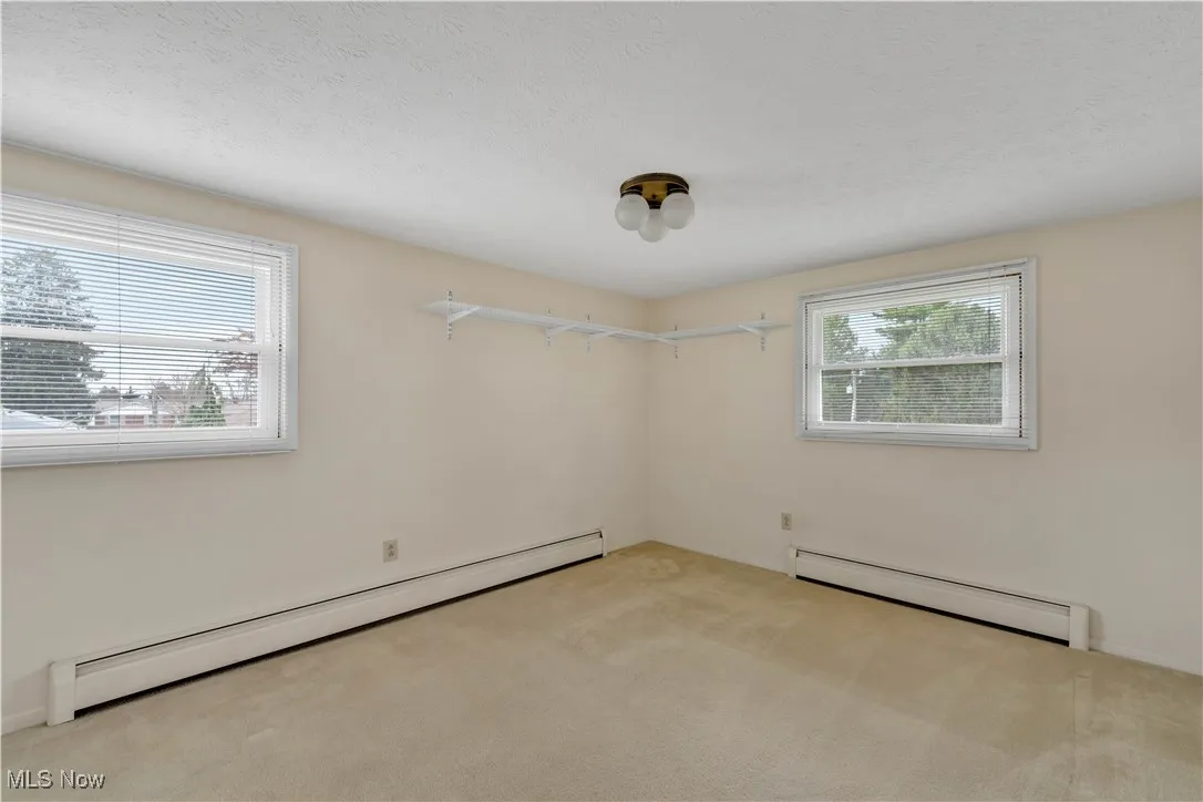 Empty room featuring a baseboard heating unit, light colored carpet, and a textured ceiling