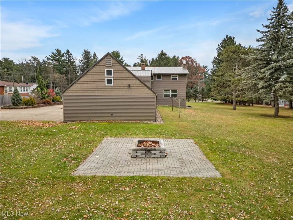 Rear view of property with a lawn, an outdoor fire pit, a chimney, and a patio area
