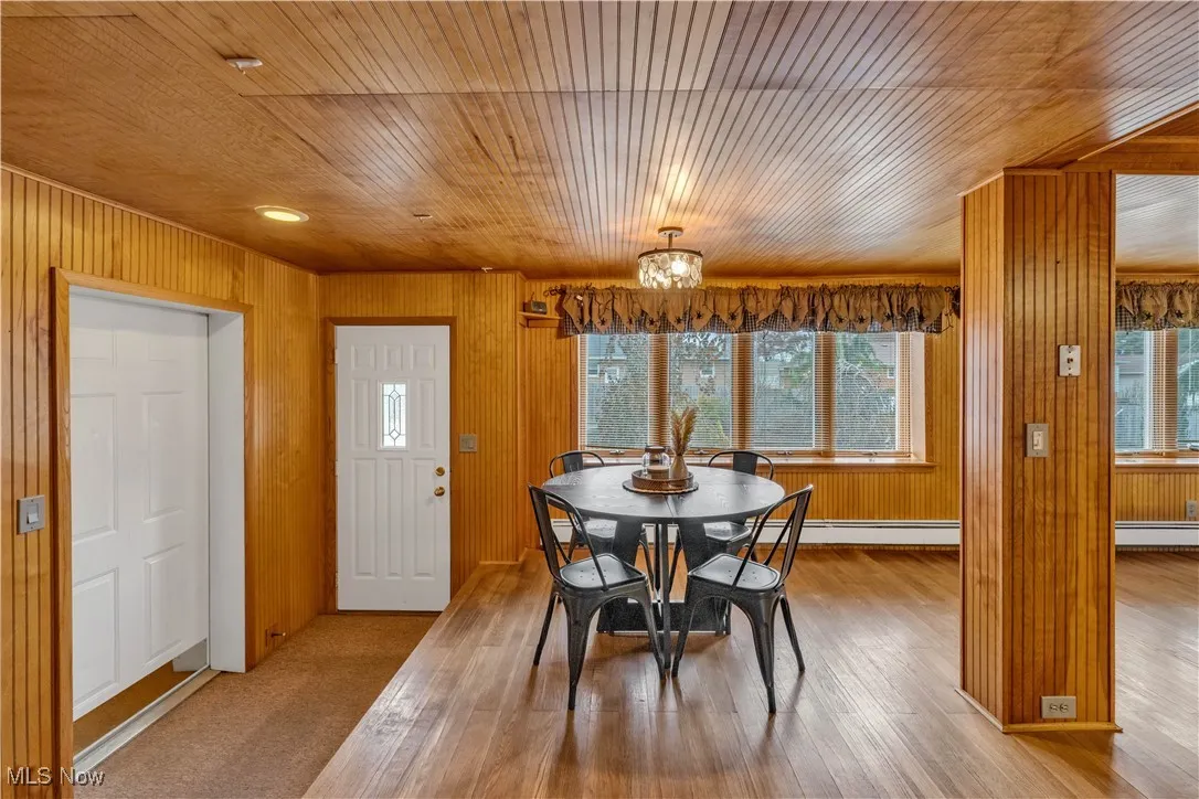 Dining area featuring wood ceiling, wood walls, a chandelier, and a baseboard radiator