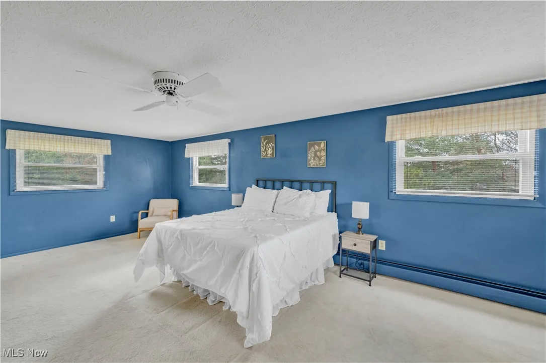 Carpeted bedroom featuring a baseboard heating unit, a textured ceiling, and a ceiling fan