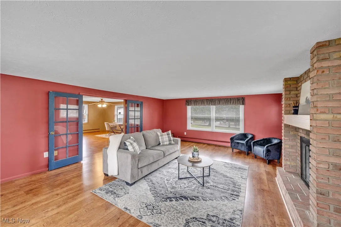 Living room with a fireplace, light wood-style flooring, plenty of natural light, a baseboard radiator, and a textured ceiling